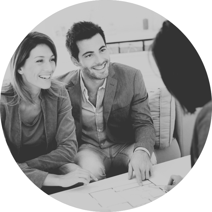 A couple sits at a table reviewing a blueprint with a professional, representing working with a granny flats builder.