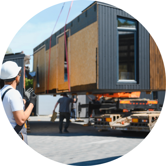 A worker in safety gear directing a crane lifting a modular building section from a truck, representing modular granny flats construction.